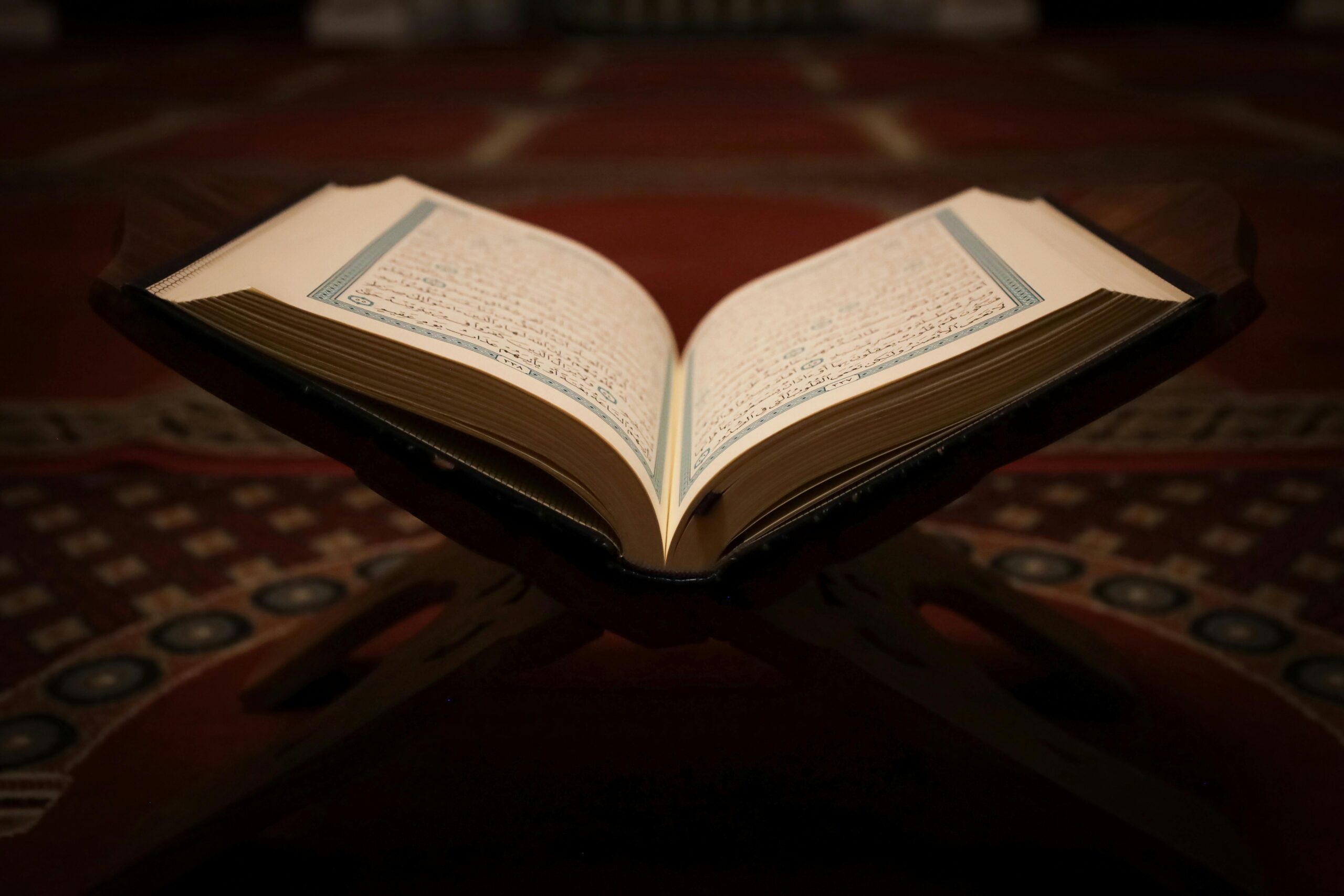 An open Quran placed on a wooden stand with mosque carpet in the background, symbolizing Islamic spirituality.
